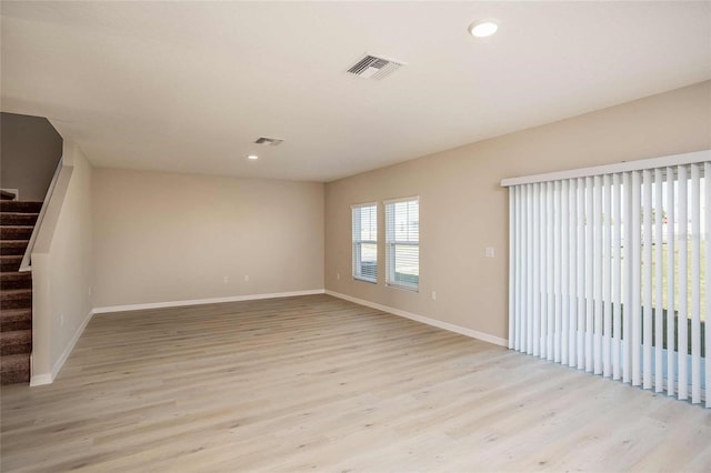 empty room featuring stairway, baseboards, visible vents, and light wood-type flooring