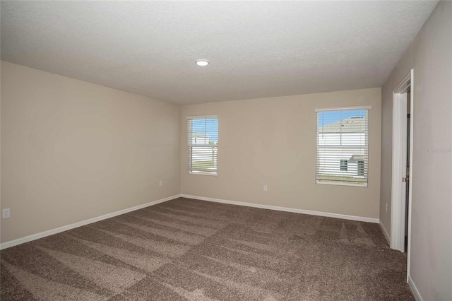 spare room featuring baseboards, dark colored carpet, and a textured ceiling