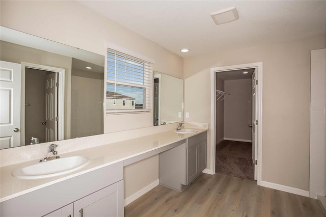 full bath with double vanity, wood finished floors, a walk in closet, and a sink