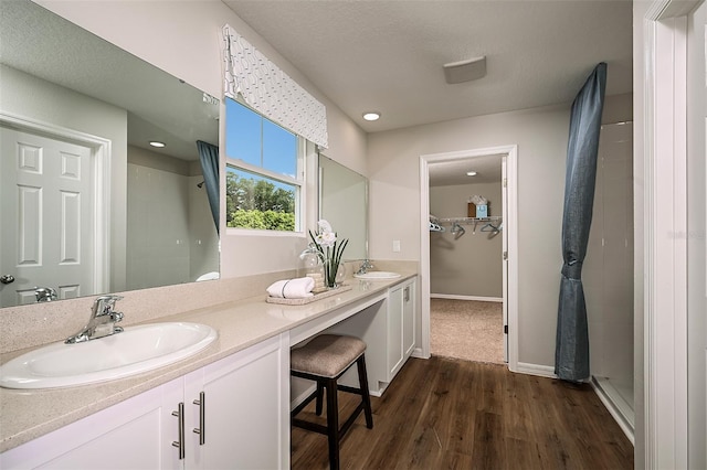 full bath featuring double vanity, tiled shower, wood finished floors, and a sink