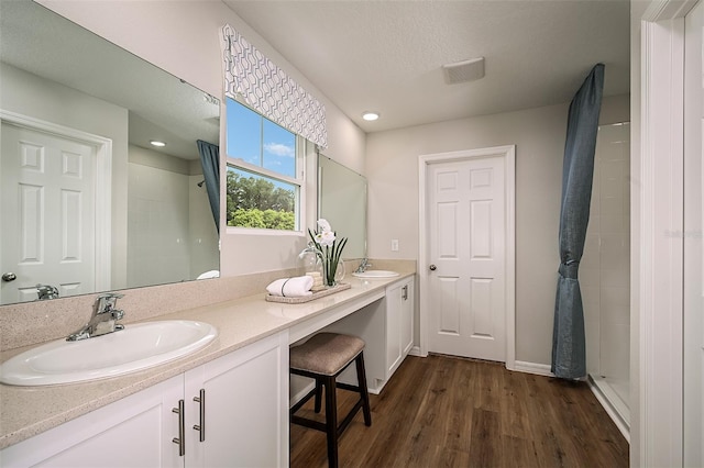 bathroom featuring double vanity, tiled shower, wood finished floors, and a sink