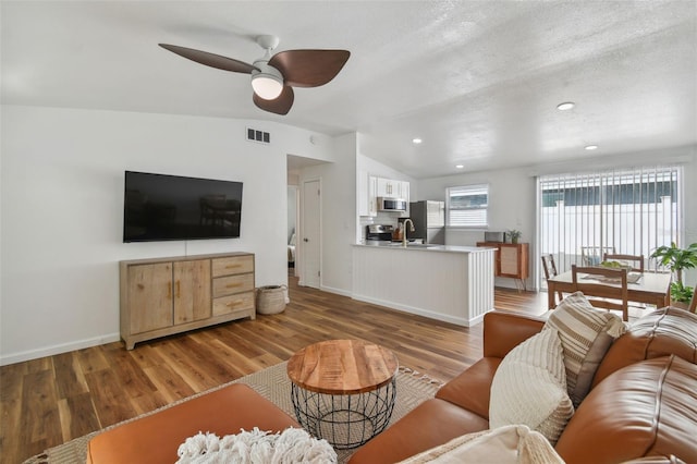 living area featuring a ceiling fan, visible vents, baseboards, lofted ceiling, and light wood-type flooring