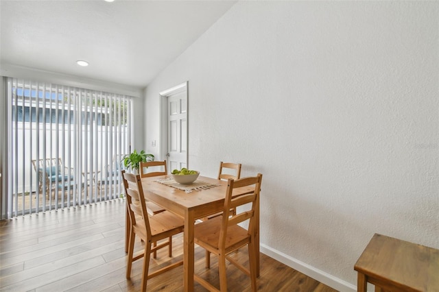 dining room featuring baseboards, lofted ceiling, wood finished floors, and a textured wall