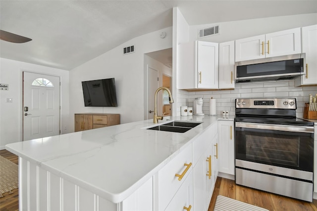 kitchen with visible vents, lofted ceiling, a peninsula, a sink, and appliances with stainless steel finishes