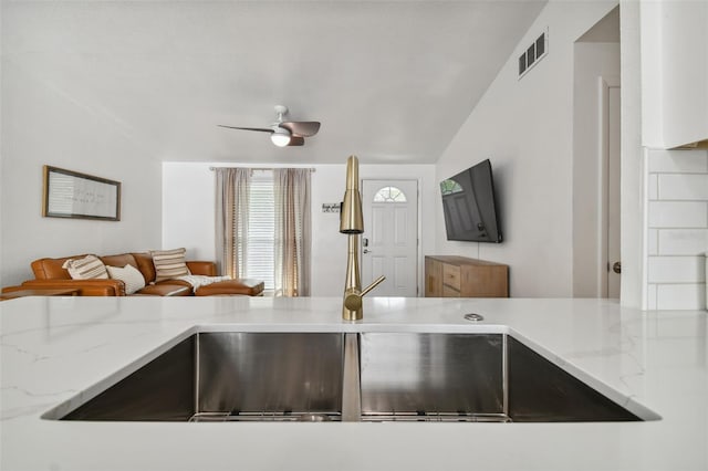 kitchen featuring light stone counters, visible vents, open floor plan, and a sink