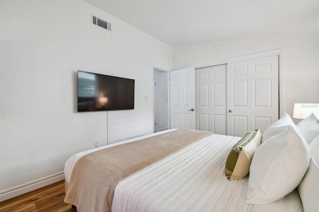 bedroom with visible vents, lofted ceiling, wood finished floors, a closet, and baseboards