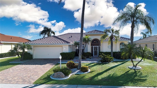 mediterranean / spanish-style house featuring a front yard, stucco siding, a garage, a tiled roof, and decorative driveway