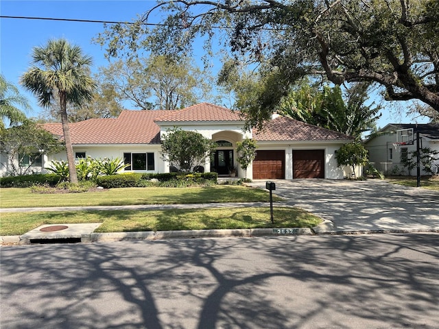 mediterranean / spanish home featuring a front lawn, a tiled roof, stucco siding, driveway, and an attached garage