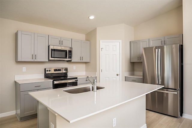 kitchen with gray cabinetry, light countertops, appliances with stainless steel finishes, light wood-style floors, and a sink