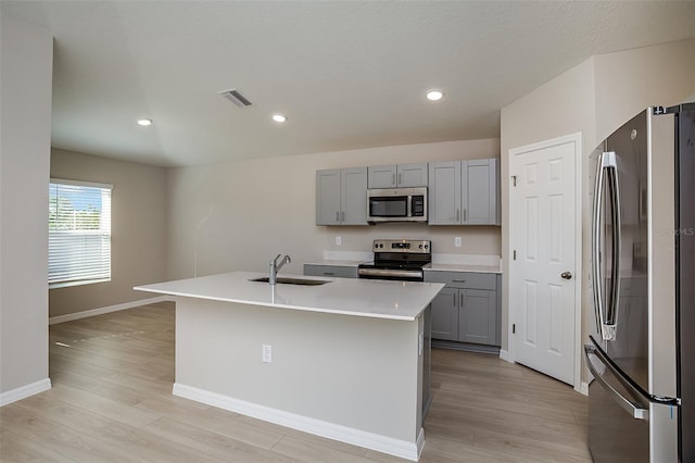 kitchen with a sink, appliances with stainless steel finishes, light wood-style flooring, and gray cabinetry