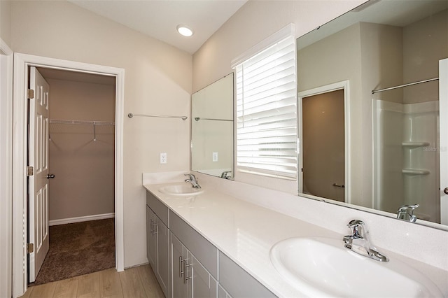 full bathroom featuring double vanity, wood finished floors, a walk in closet, and a sink