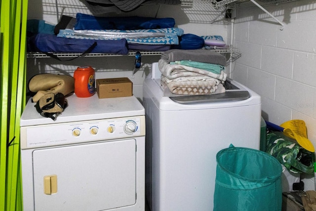 clothes washing area featuring independent washer and dryer and concrete block wall