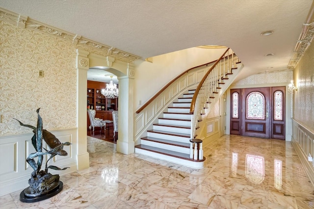 foyer entrance with wallpapered walls, a decorative wall, a notable chandelier, and marble finish floor