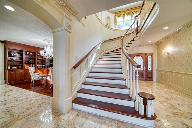 staircase featuring a wainscoted wall, a notable chandelier, marble finish floor, a textured ceiling, and a decorative wall