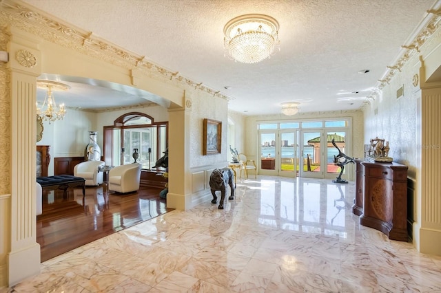 interior space with a notable chandelier, marble finish floor, a textured ceiling, arched walkways, and crown molding