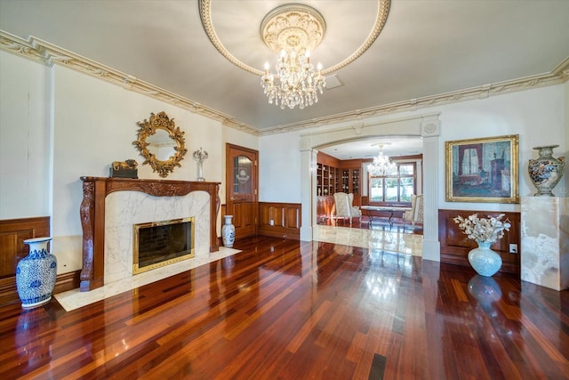 living room with wood finished floors, a fireplace, arched walkways, ornamental molding, and a chandelier