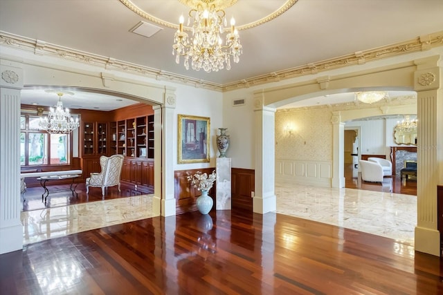interior space with wood finished floors, arched walkways, an inviting chandelier, wainscoting, and a decorative wall