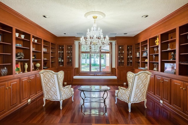 sitting room with a chandelier, dark wood finished floors, a textured ceiling, and ornamental molding