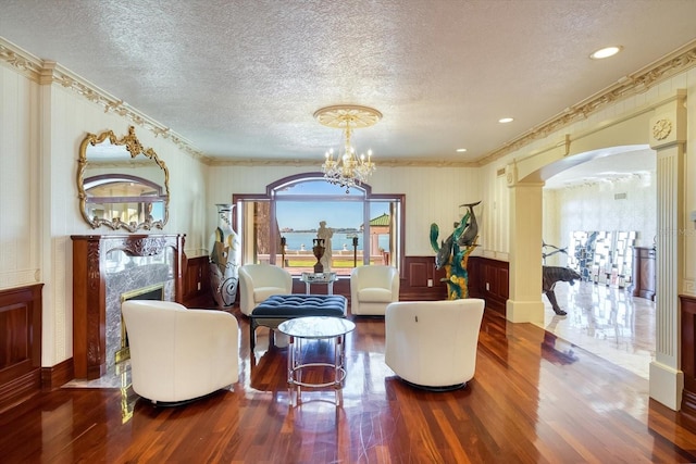 sitting room with wood finished floors, an inviting chandelier, decorative columns, arched walkways, and a high end fireplace