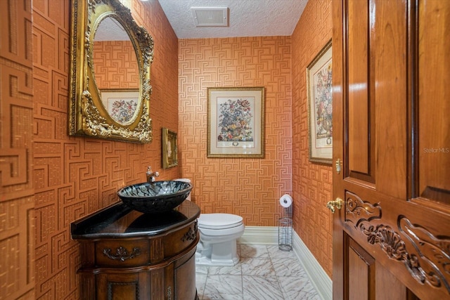 bathroom with visible vents, baseboards, toilet, marble finish floor, and a textured ceiling