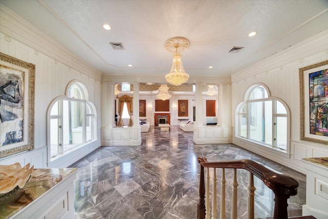 foyer with visible vents, crown molding, a decorative wall, marble finish floor, and ornate columns