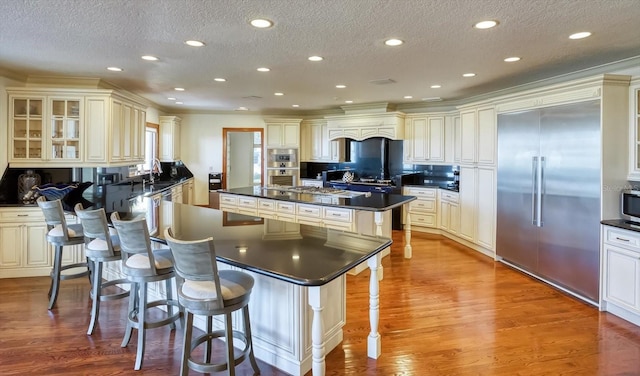 kitchen featuring a sink, a kitchen island, dark countertops, wood finished floors, and appliances with stainless steel finishes