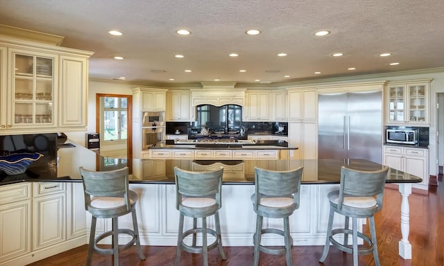 kitchen featuring stainless steel appliances, cream cabinets, dark countertops, and dark wood finished floors