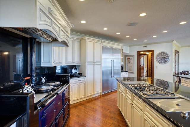 kitchen featuring dark countertops, dark wood finished floors, appliances with stainless steel finishes, custom exhaust hood, and cream cabinetry