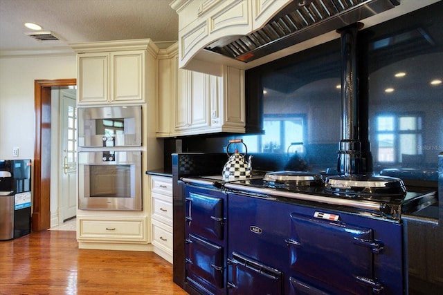 kitchen with visible vents, custom exhaust hood, cream cabinetry, dark countertops, and light wood-type flooring