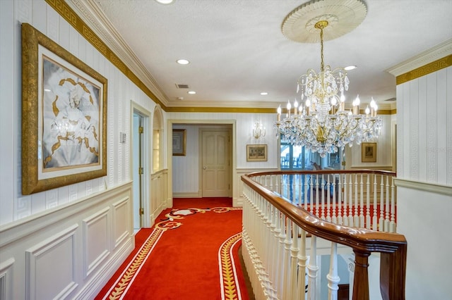 hallway featuring wallpapered walls, ornamental molding, wainscoting, dark carpet, and a chandelier