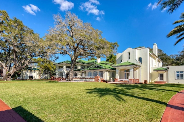 back of house featuring a lawn, a chimney, and stucco siding