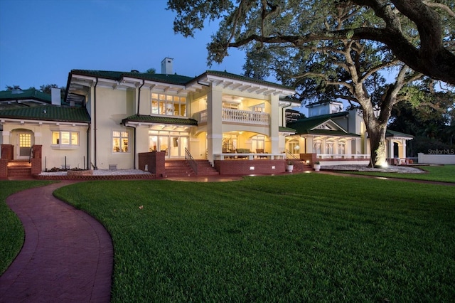rear view of property with a yard, stucco siding, brick siding, and a balcony