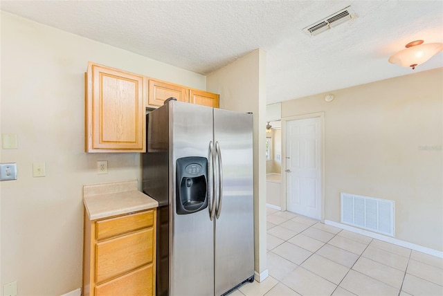 kitchen featuring light tile patterned flooring, visible vents, stainless steel fridge, and light brown cabinetry