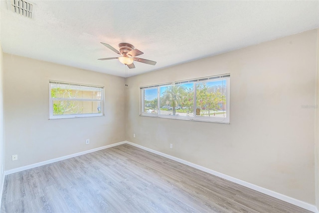 unfurnished room featuring a wealth of natural light, visible vents, baseboards, and a ceiling fan