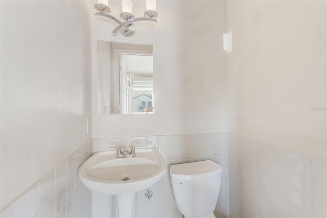 bathroom featuring a sink, a wainscoted wall, toilet, and tile walls