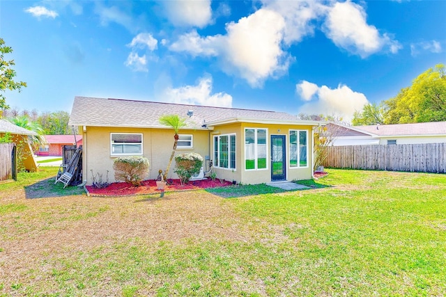 back of property with stucco siding, a lawn, and fence