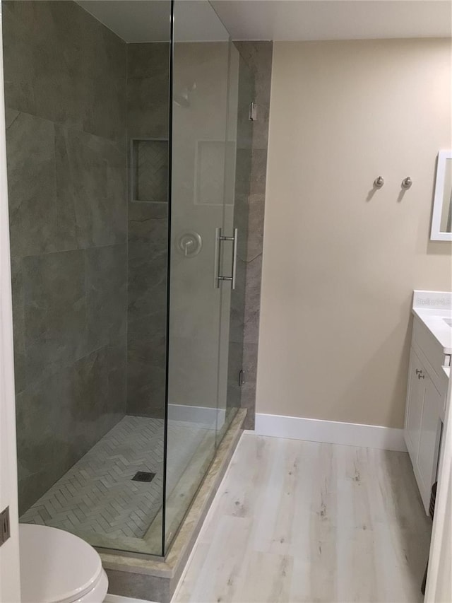 full bathroom with toilet, wood finished floors, a shower stall, baseboards, and vanity