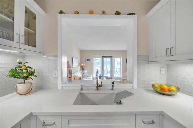 kitchen with white cabinets, light countertops, glass insert cabinets, and a sink