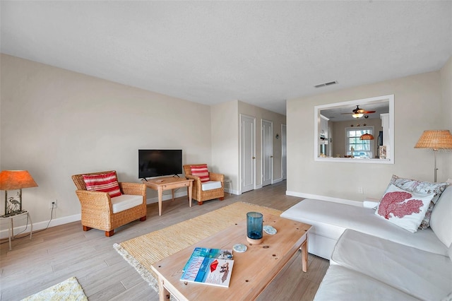 living area with visible vents, baseboards, wood finished floors, a textured ceiling, and a ceiling fan