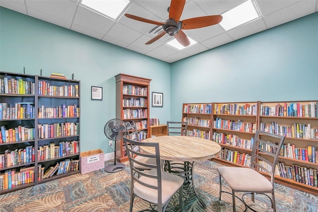 office space featuring a paneled ceiling, wall of books, baseboards, and ceiling fan