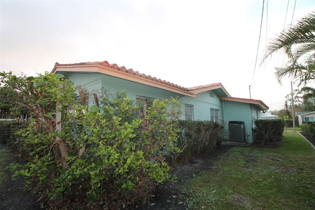 view of property exterior featuring central AC unit, a tiled roof, and a yard