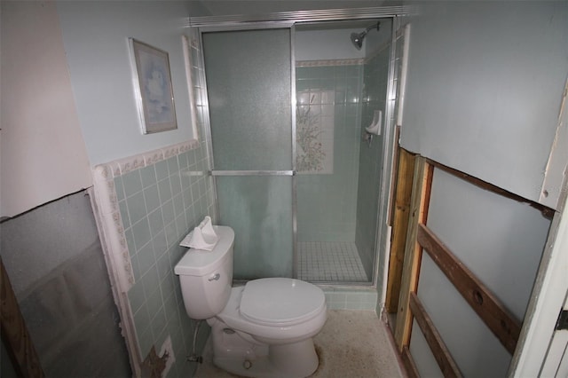 bathroom featuring a wainscoted wall, tile walls, toilet, and a stall shower