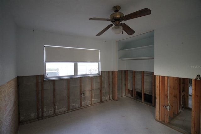 unfurnished room featuring a wainscoted wall, concrete floors, and ceiling fan