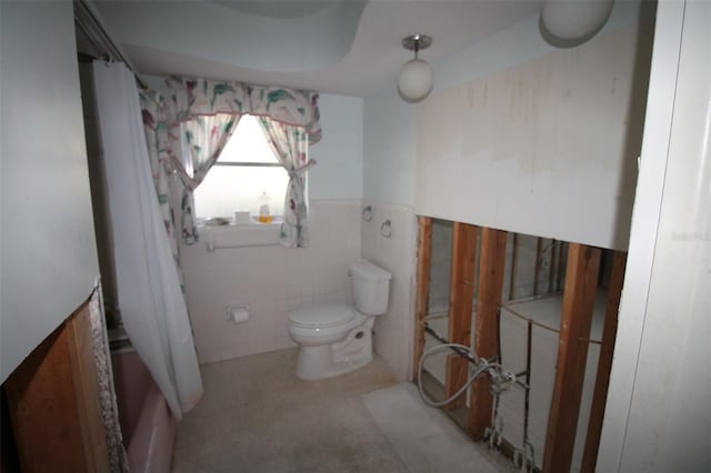 bathroom with tile walls, toilet, and a wainscoted wall