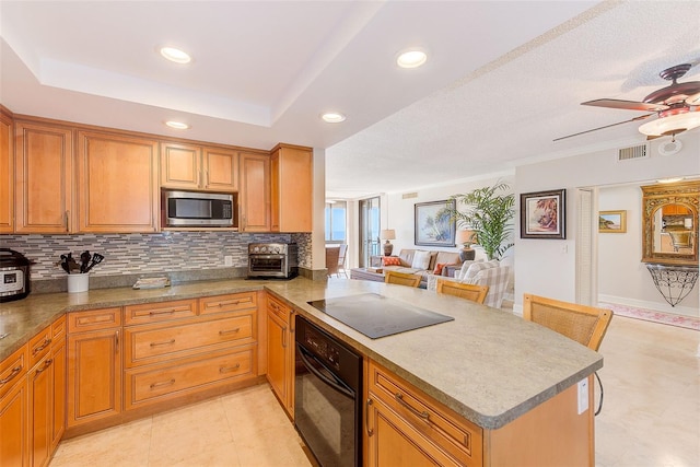 kitchen with visible vents, a peninsula, black appliances, a raised ceiling, and a ceiling fan