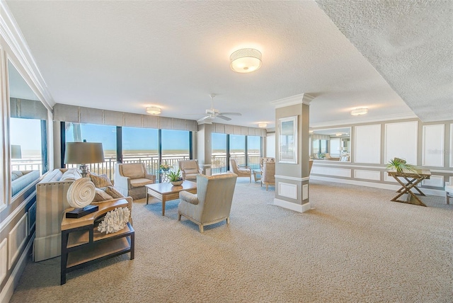 carpeted living area featuring ceiling fan, a decorative wall, ornamental molding, and a textured ceiling