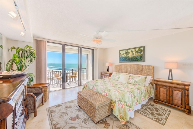 bedroom with a water view, track lighting, access to outside, expansive windows, and ceiling fan