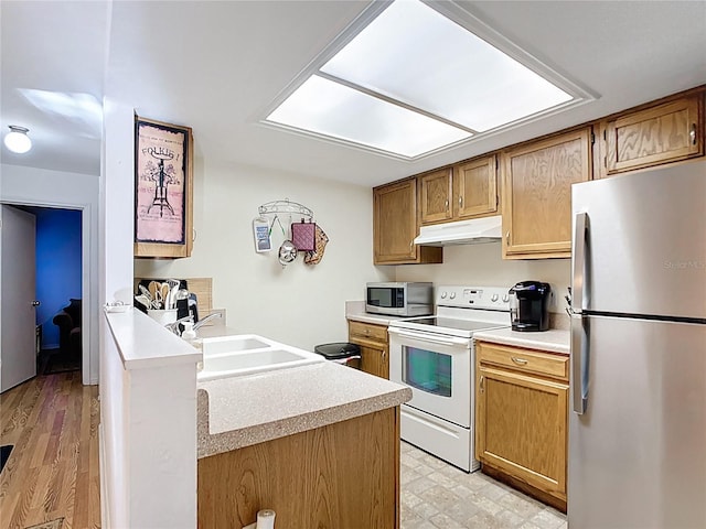 kitchen with light floors, a peninsula, a sink, under cabinet range hood, and appliances with stainless steel finishes