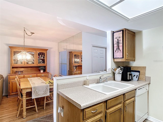 kitchen with pendant lighting, light wood-style flooring, a sink, light countertops, and dishwasher