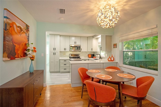 dining room featuring visible vents, baseboards, a chandelier, light wood-style floors, and a textured ceiling